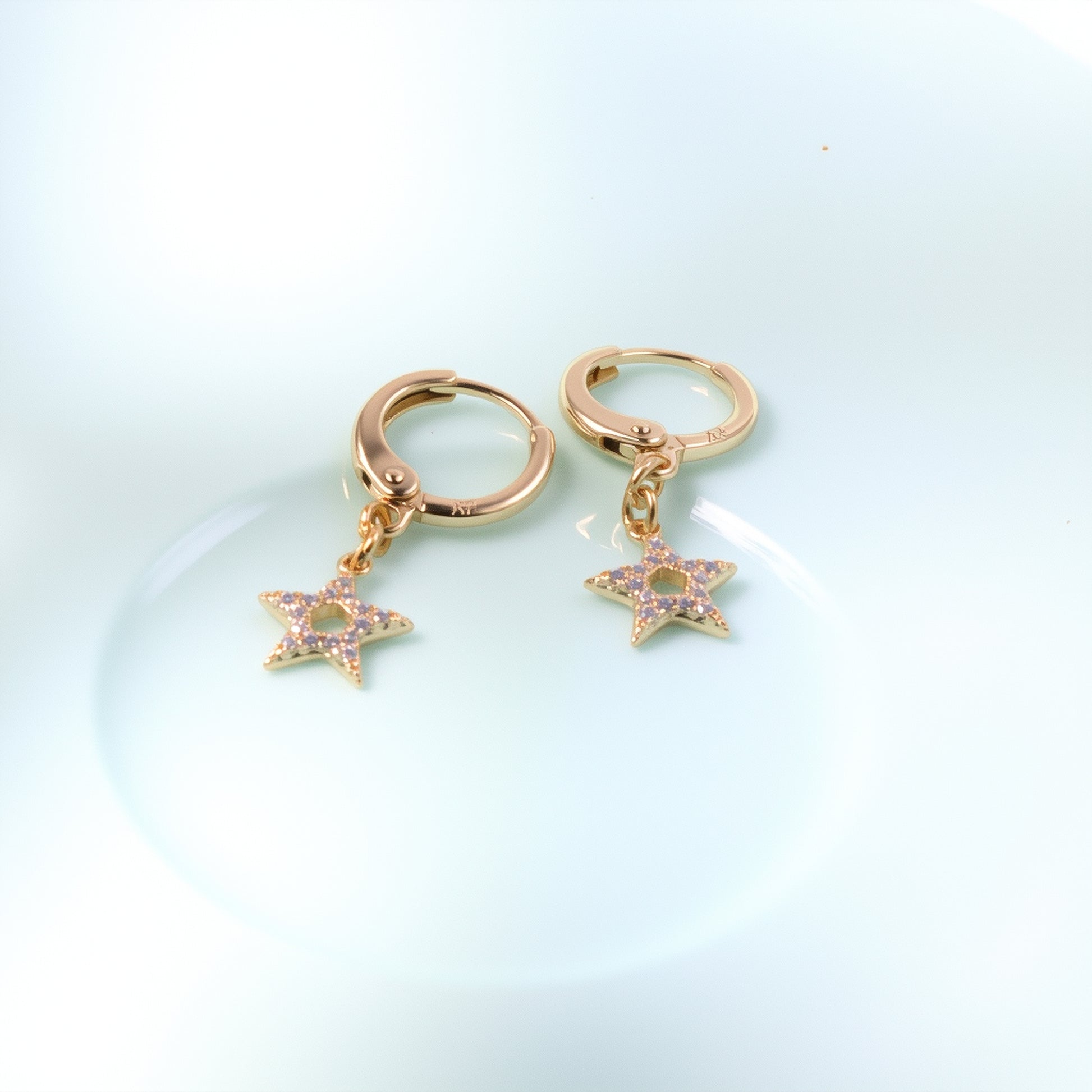 Delicate 14K gold huggie hoop earrings with a mini dangling star charm