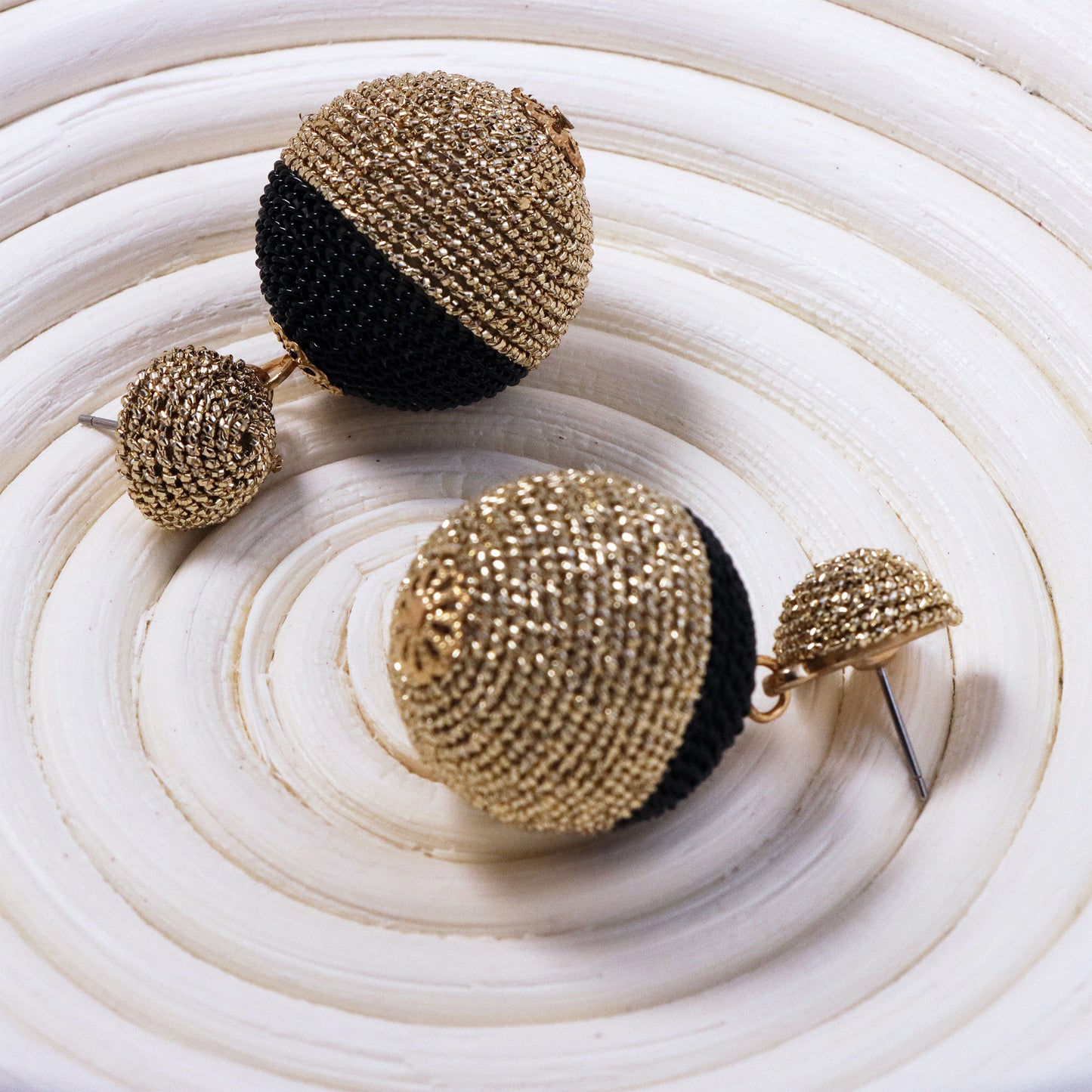 Macro shot of two rattan straw spheres with natural grain texture, dangling from gold chains against a sunset-hued textile