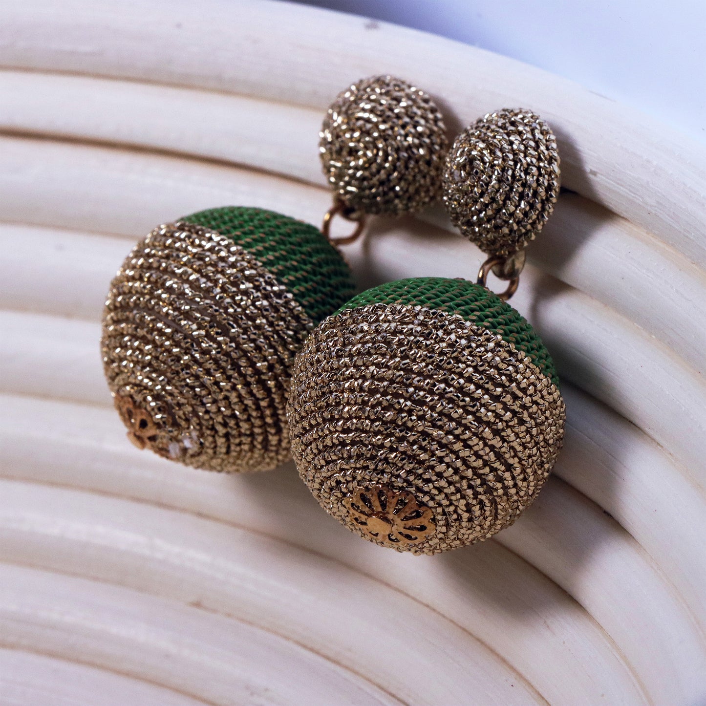 Macro shot of two rattan straw spheres with natural grain texture, dangling from gold chains against a sunset-hued textile