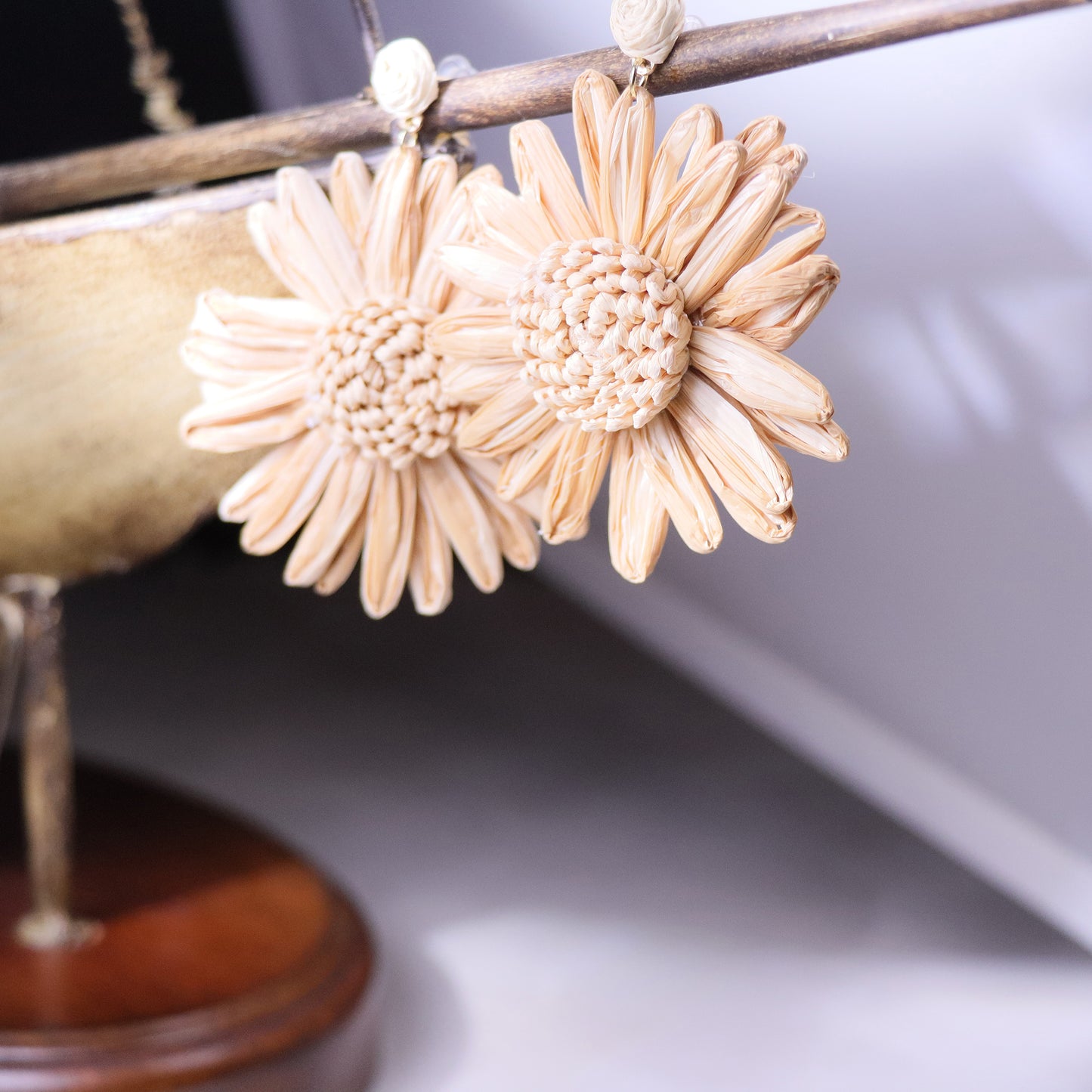 Macro shot of rattan sunflower earrings with layered petals and brass accents, displayed on a bed of dried wheat stalks.