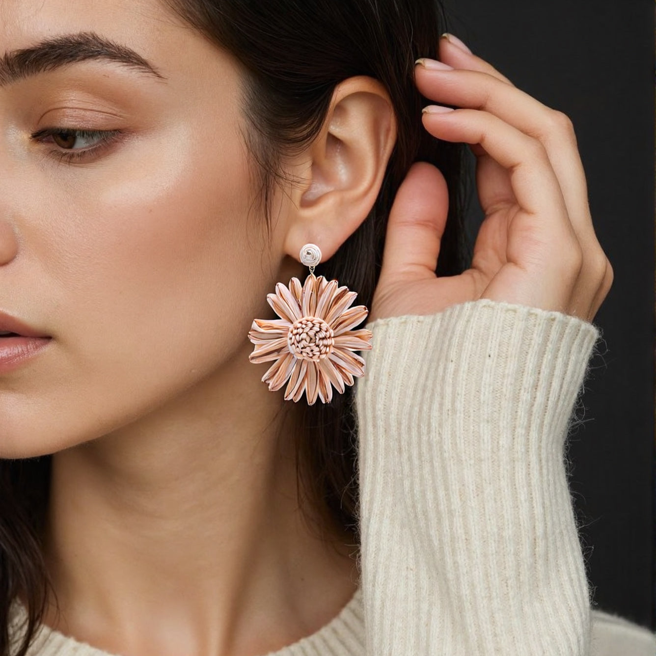 Macro shot of rattan sunflower earrings with layered petals and brass accents, displayed on a bed of dried wheat stalks.