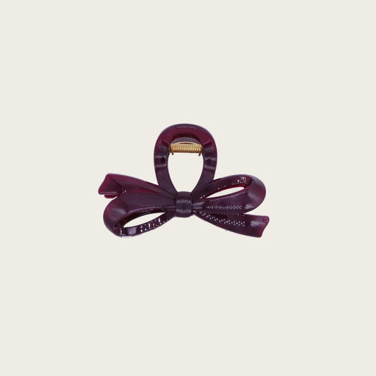 Deep burgundy bow-shaped claw clip with wide teeth, holding a voluminous low bun on dark hair.