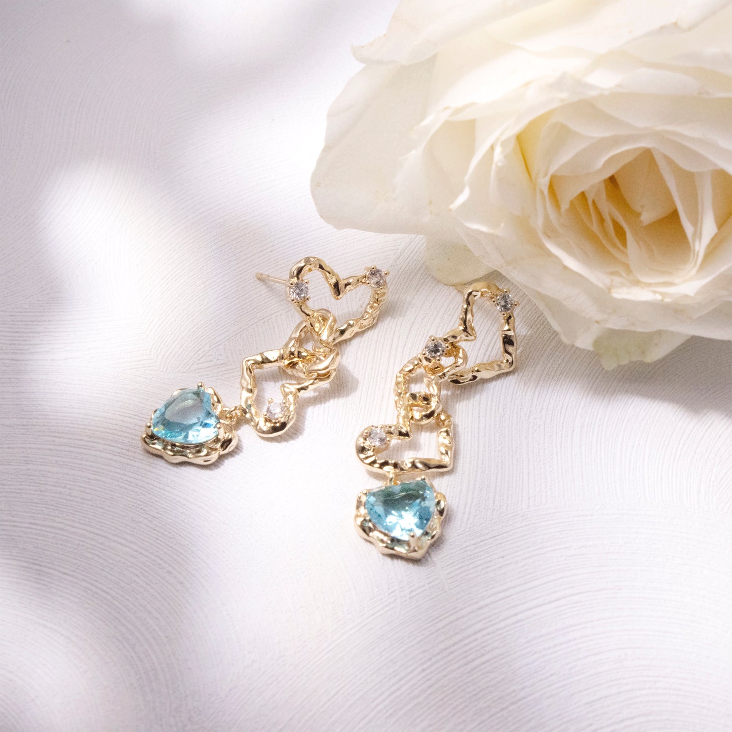 Ocean-blue crystal heart dangle earrings with 14K gold plating, featuring sparkling faceted stones in a romantic heart silhouette
