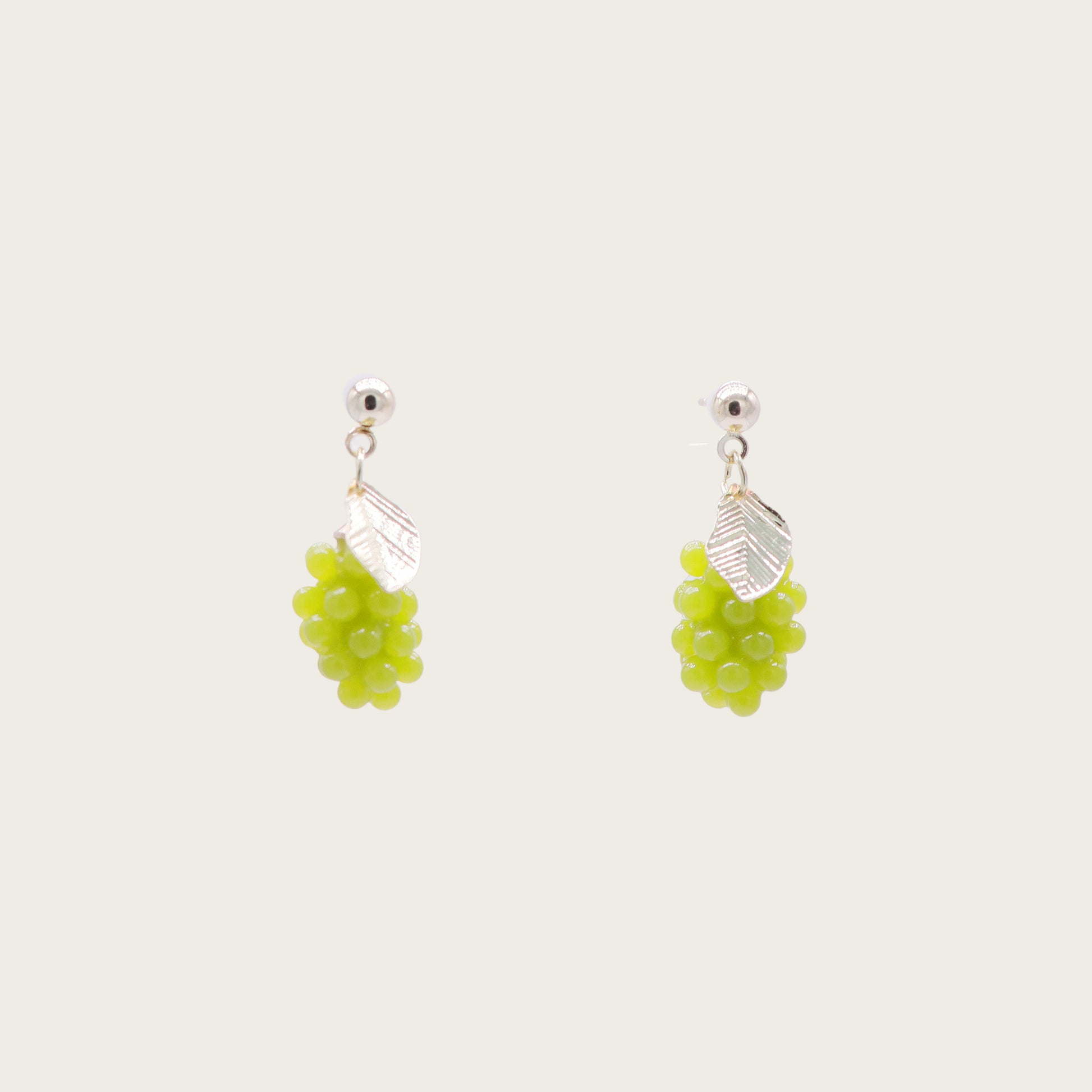 Close-up of translucent green grape cluster earrings with gold vine detailing, displayed on a marble surface with fresh grape