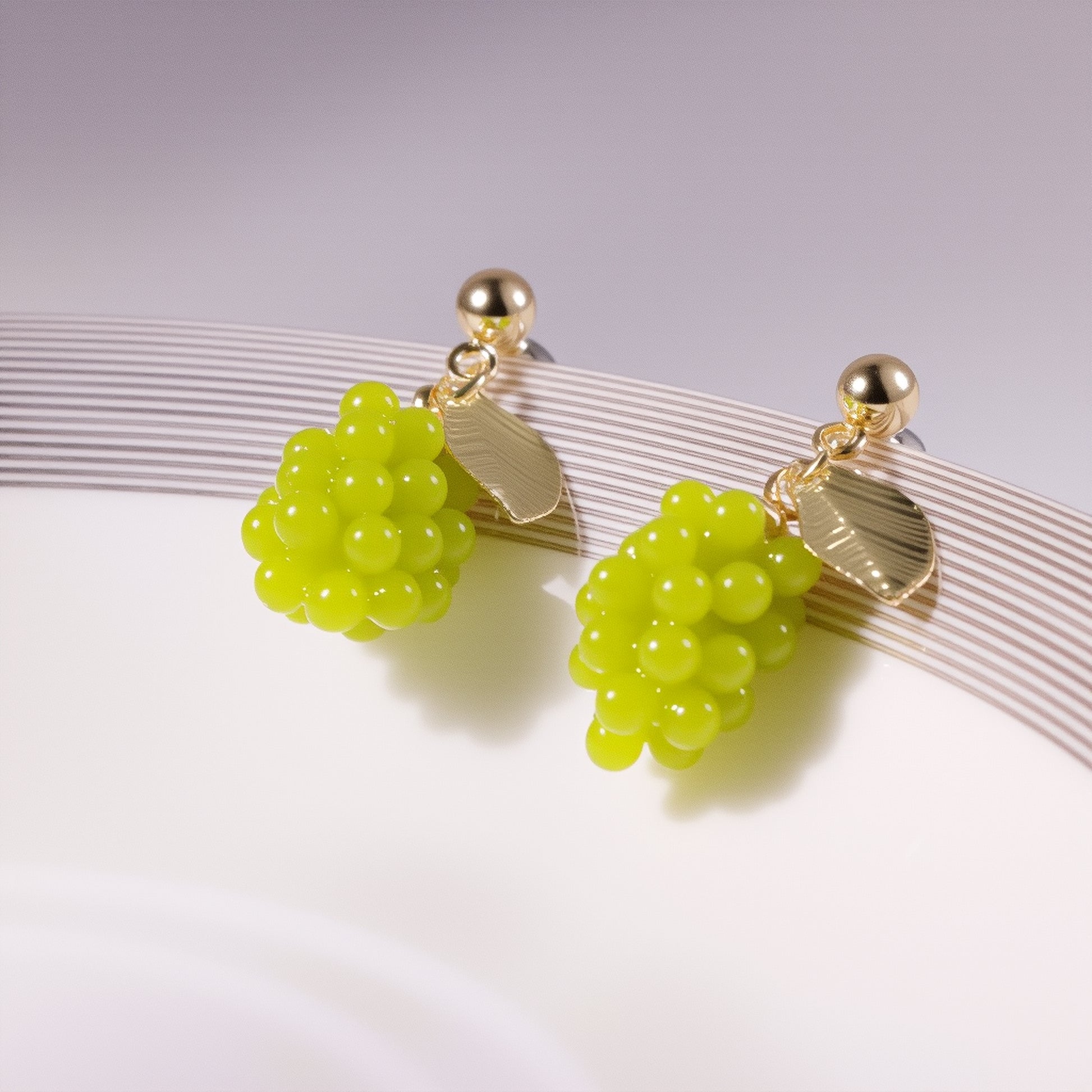 Close-up of translucent green grape cluster earrings with gold vine detailing, displayed on a marble surface with fresh grape