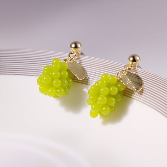 Close-up of translucent green grape cluster earrings with gold vine detailing, displayed on a marble surface with fresh grape