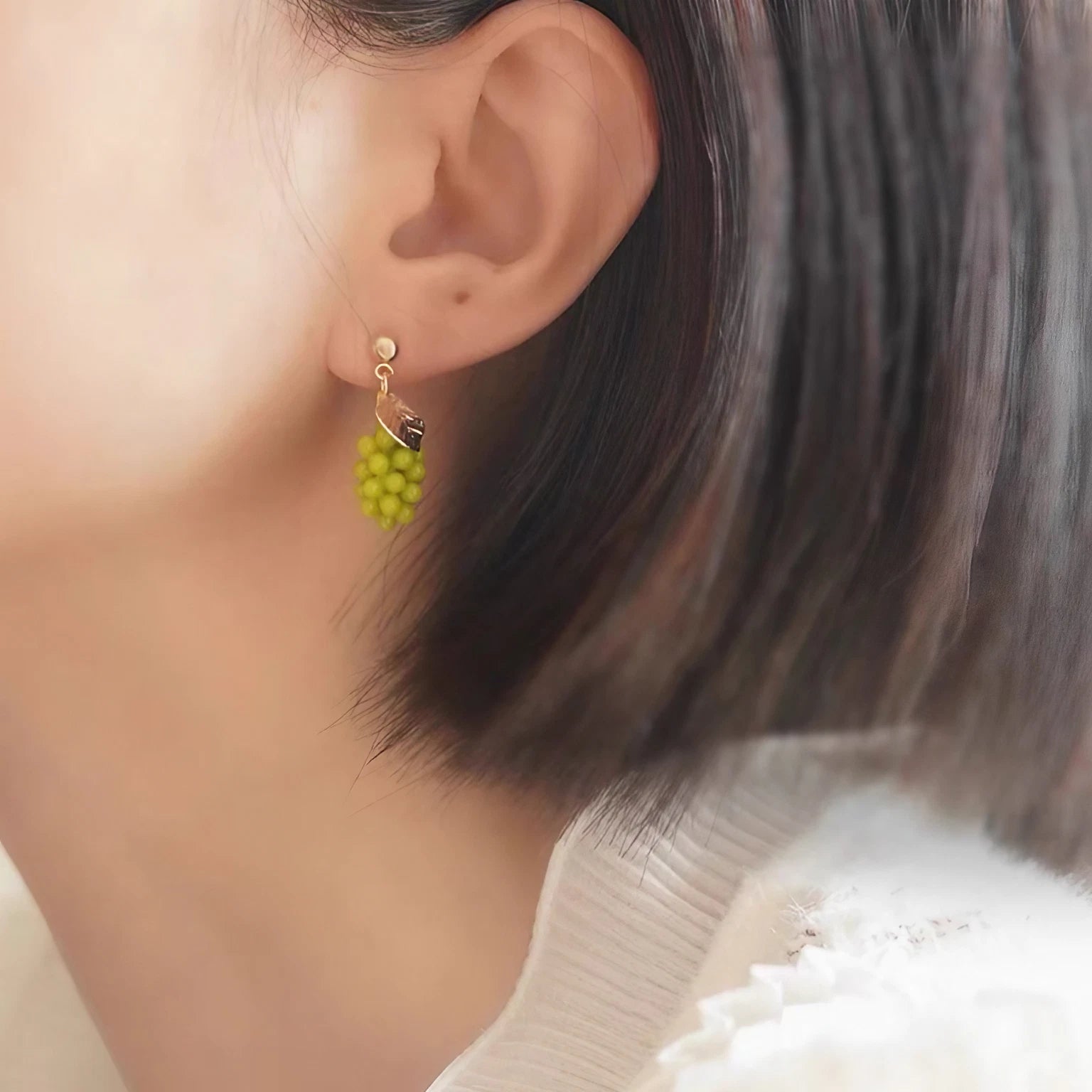 Close-up of translucent green grape cluster earrings with gold vine detailing, displayed on a marble surface with fresh grape