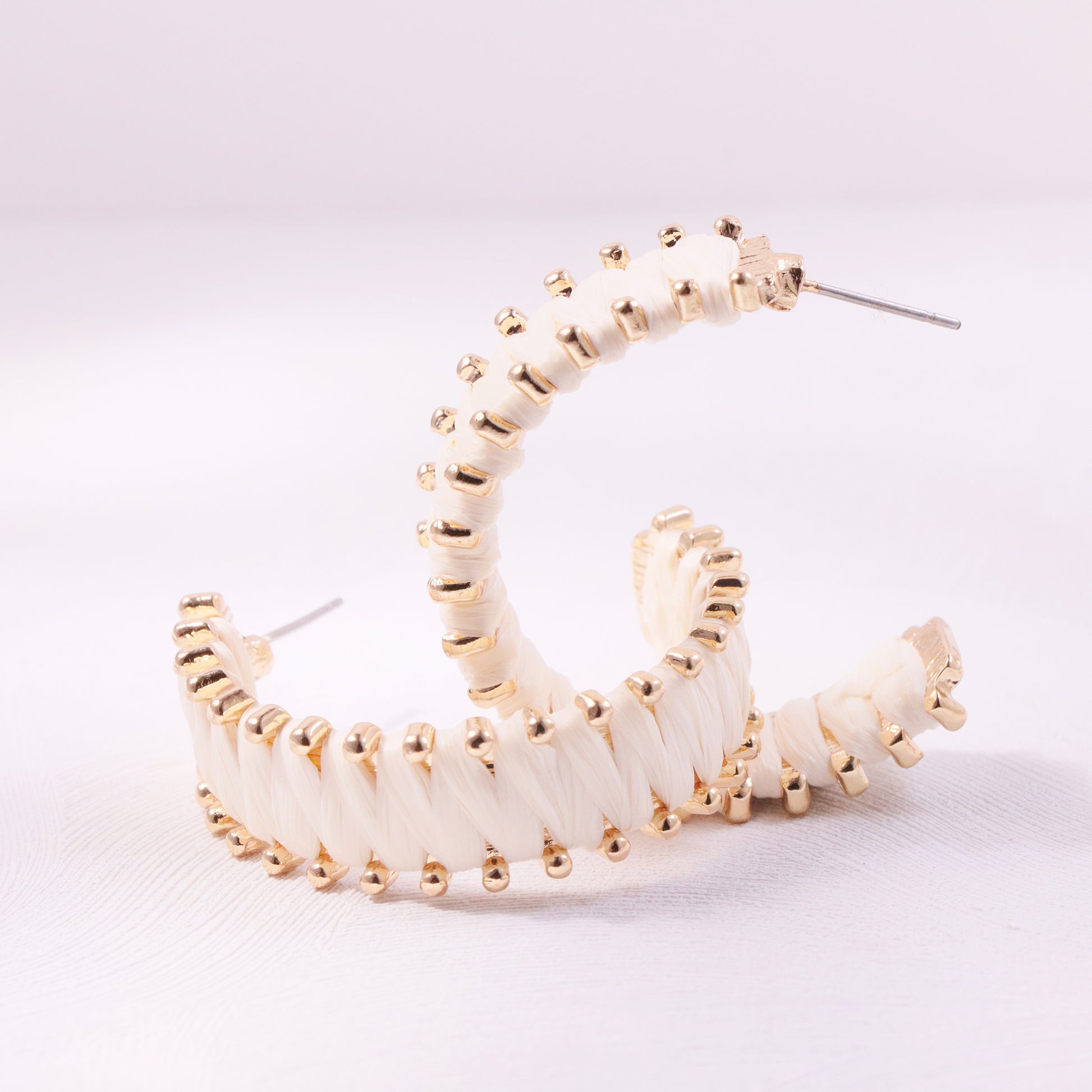 Close-up of circular woven rattan earrings with brass accents, modeled on a woman with tousled beach waves.