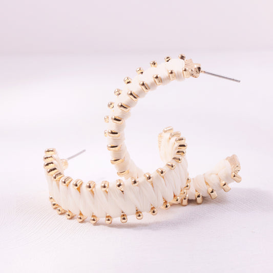 Close-up of circular woven rattan earrings with brass accents, modeled on a woman with tousled beach waves.