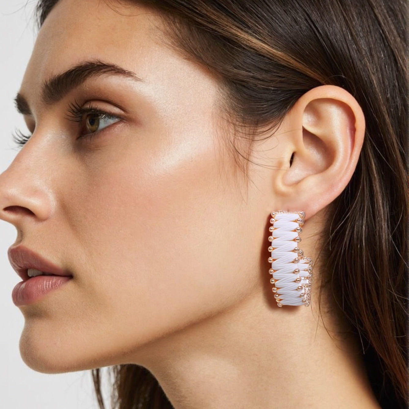 Close-up of circular woven rattan earrings with brass accents, modeled on a woman with tousled beach waves.
