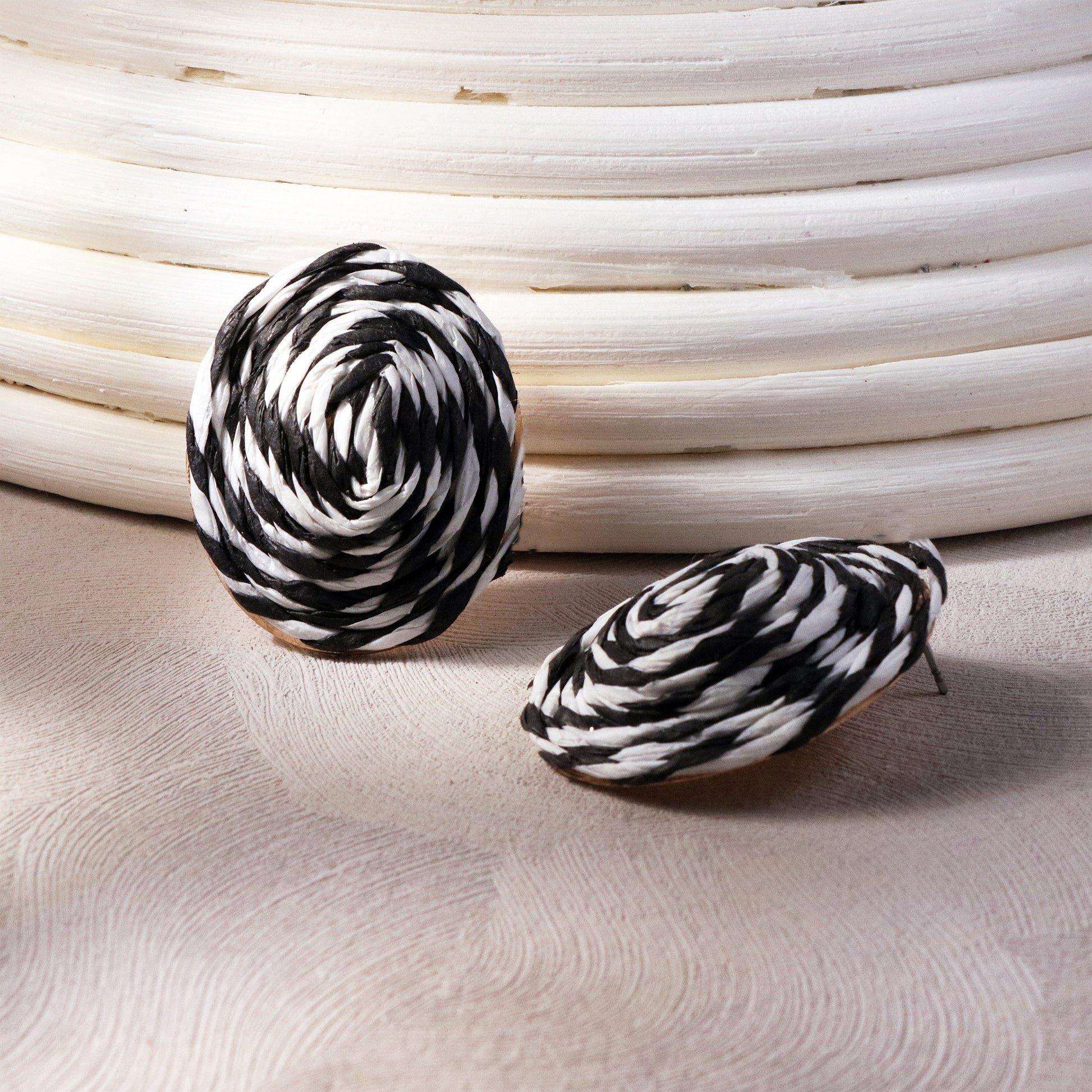Close-up of circular black and white rattan stud earrings with intricate woven texture