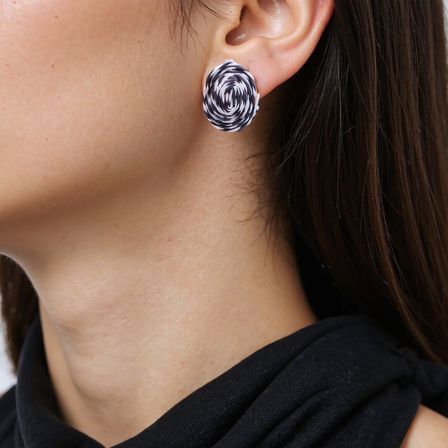 Close-up of circular black and white rattan stud earrings with intricate woven texture