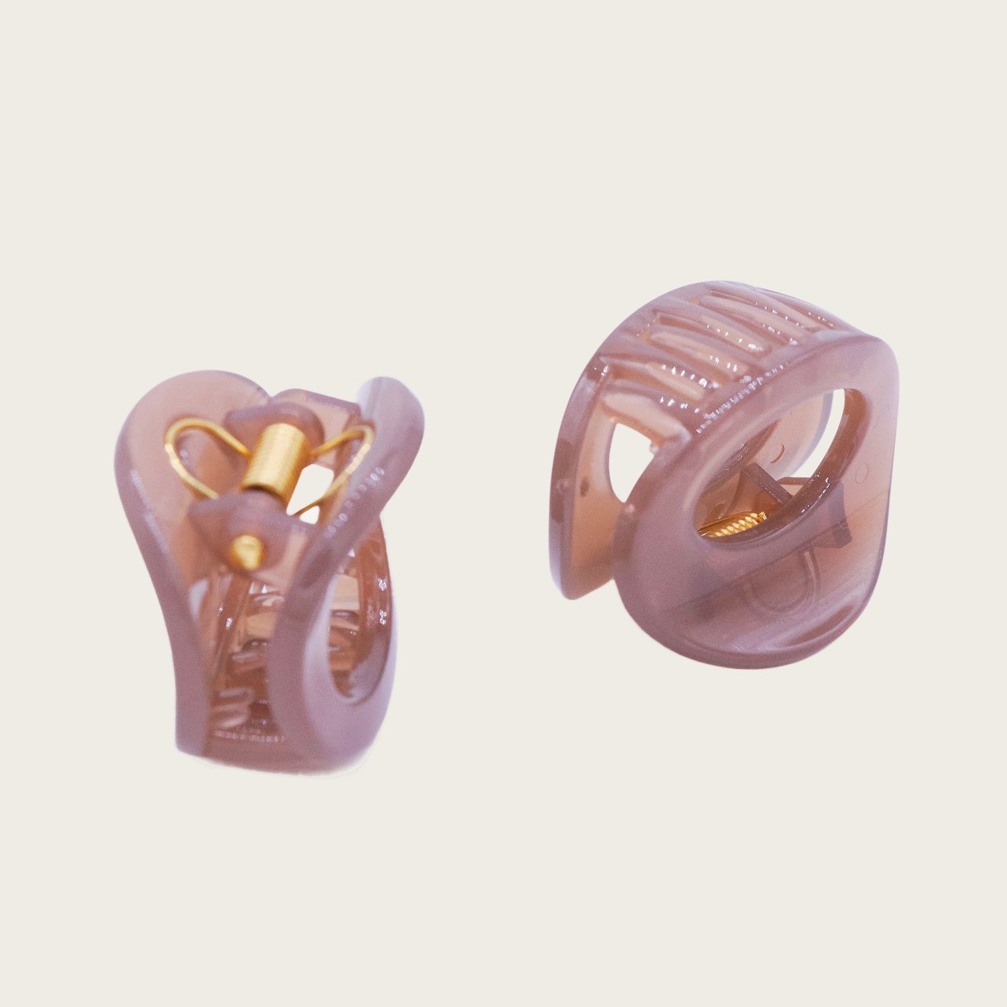 Petite oval hair claw clip in beige, holding a twisted section of blonde hair against a neutral background.