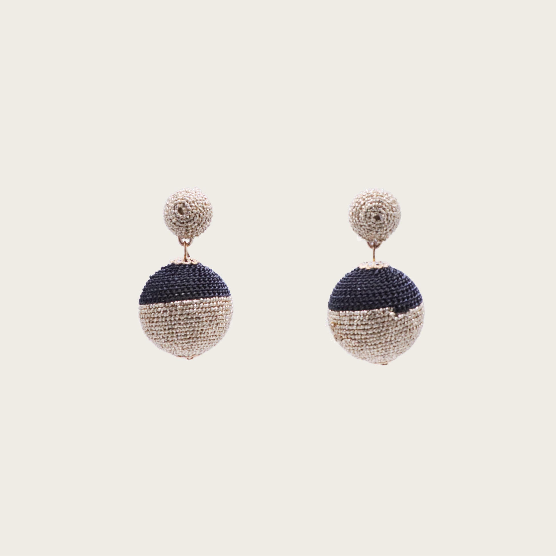 Macro shot of two rattan straw spheres with natural grain texture, dangling from gold chains against a sunset-hued textile