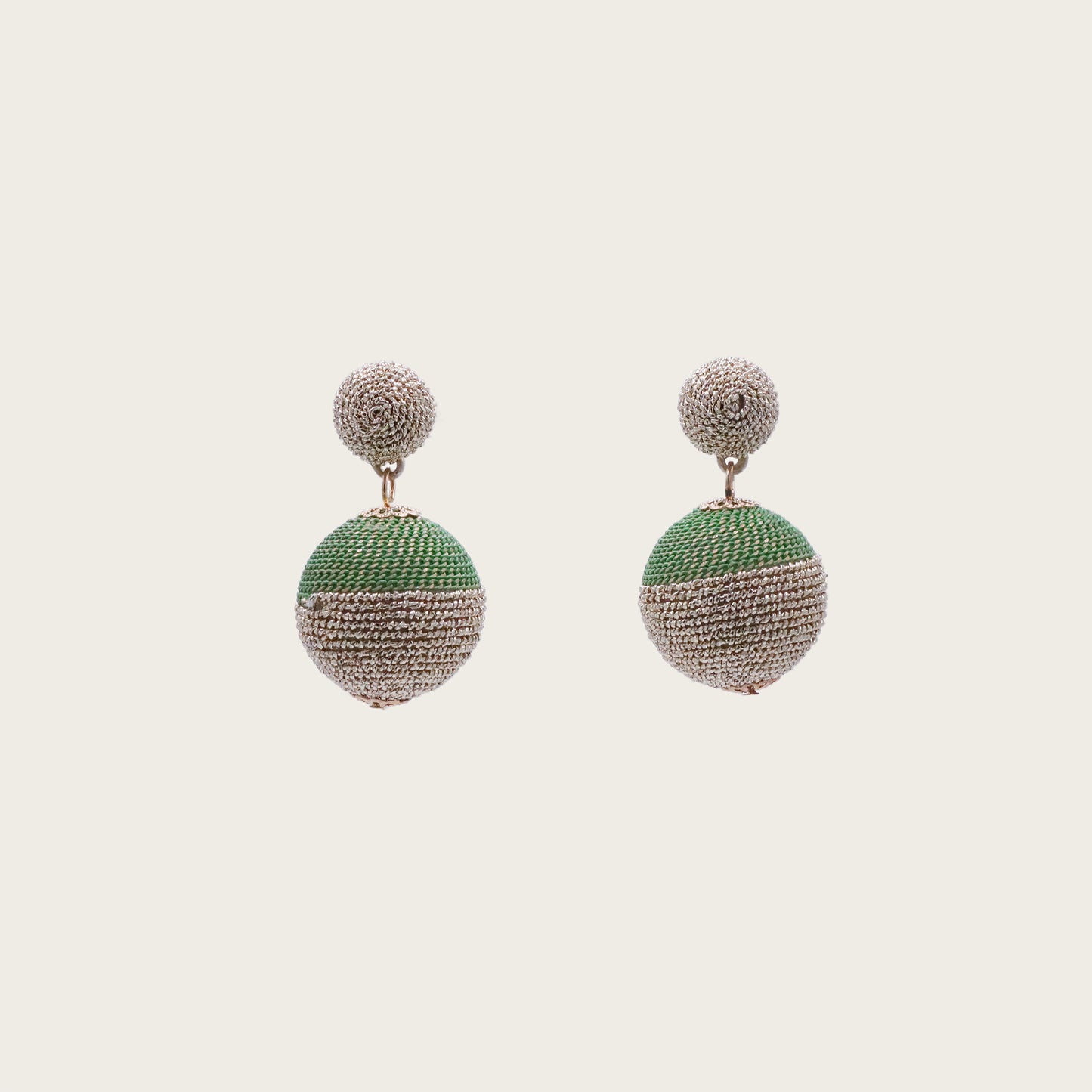 Macro shot of two rattan straw spheres with natural grain texture, dangling from gold chains against a sunset-hued textile